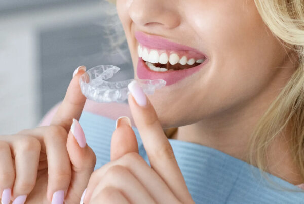 Smiling woman holding clear aligner in front of her mouth.