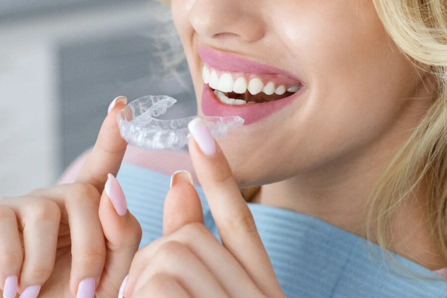 Smiling woman holding clear aligner in front of her mouth.