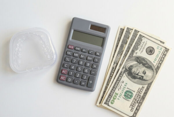 Clear dental aligners next to a calculator and cash showing orthodontic treatment costs.