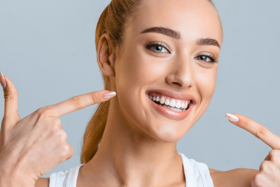 Smiling woman pointing to her bright, healthy, and professional teeth whitening results.